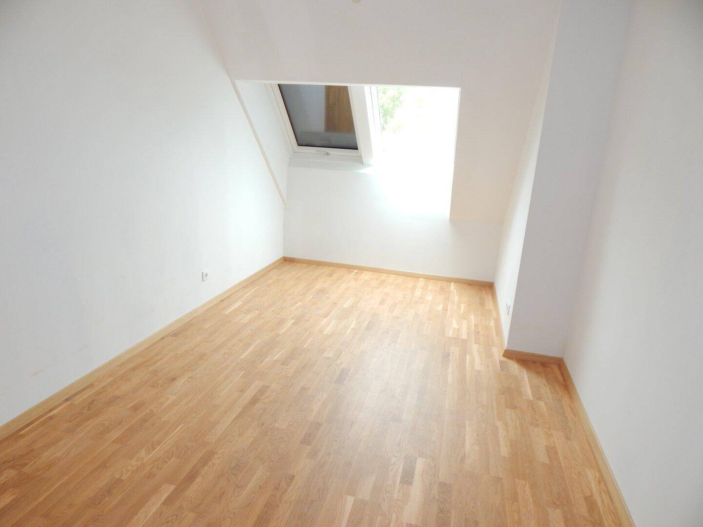 Helles Schlafzimmer mit Holzboden und Dachfenster, ideal für ein Kinder- oder Gästezimmer.