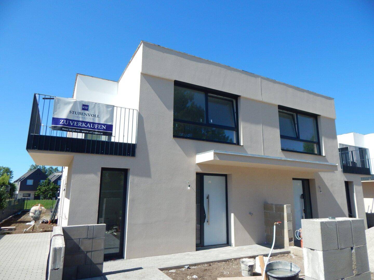 Moderne Doppelhaushälfte im Bau mit klaren Linien und Balkonen unter blauem Himmel.