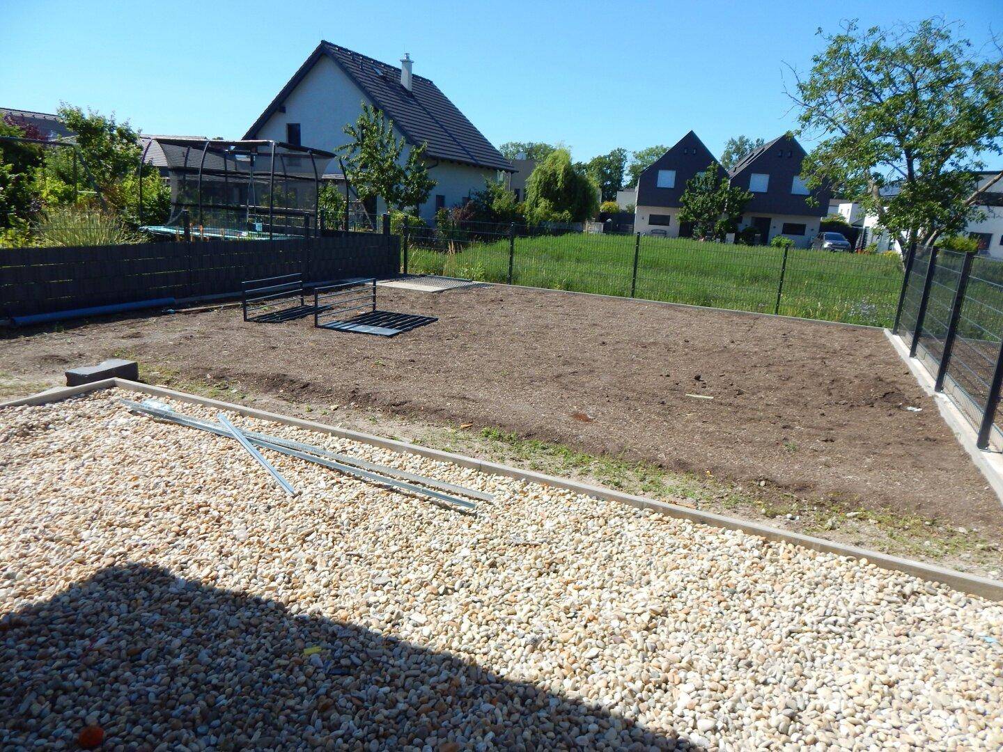 Neu angelegter Gartenbereich mit Kiesfläche und vorbereitetem Boden für Rasen, umgeben von Zäunen.