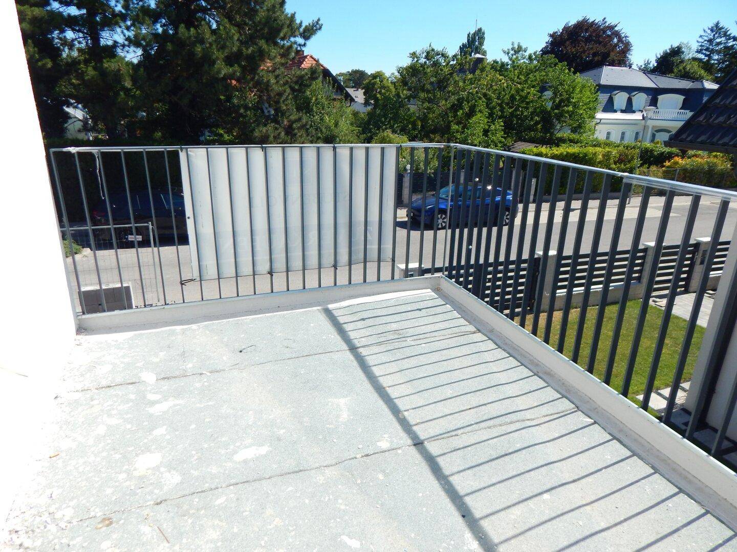 Blick von einem Balkon auf die Straße und die umliegende Wohngegend mit Bäumen.