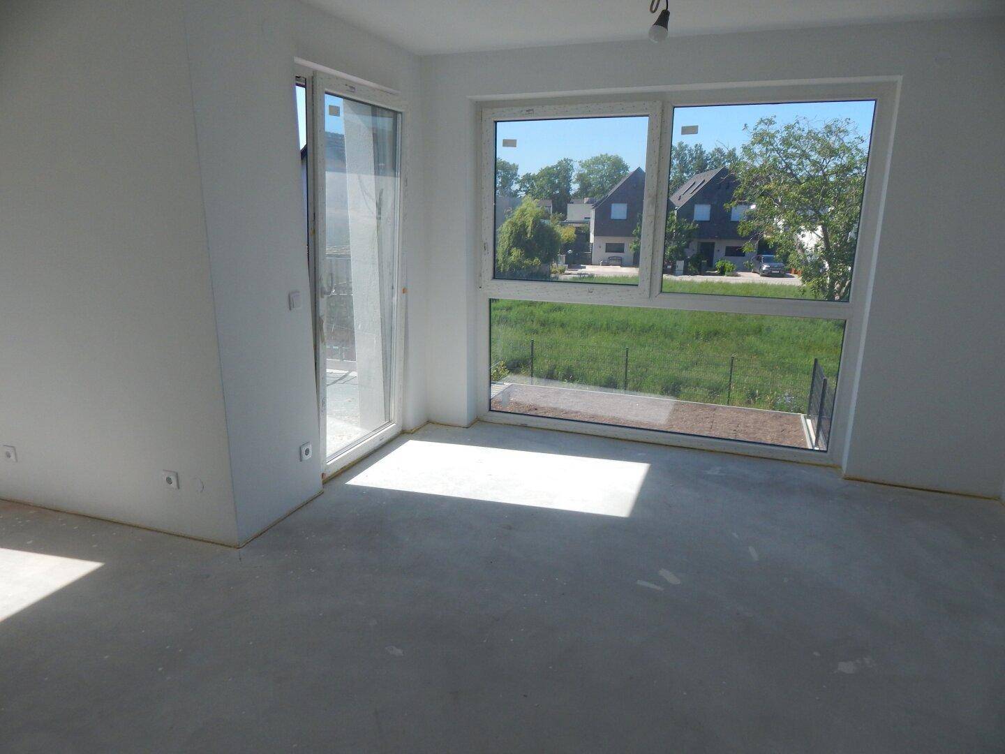Heller, unmöblierter Raum mit großen Fenstern und Zugang zu einem zukünftigen Balkon.