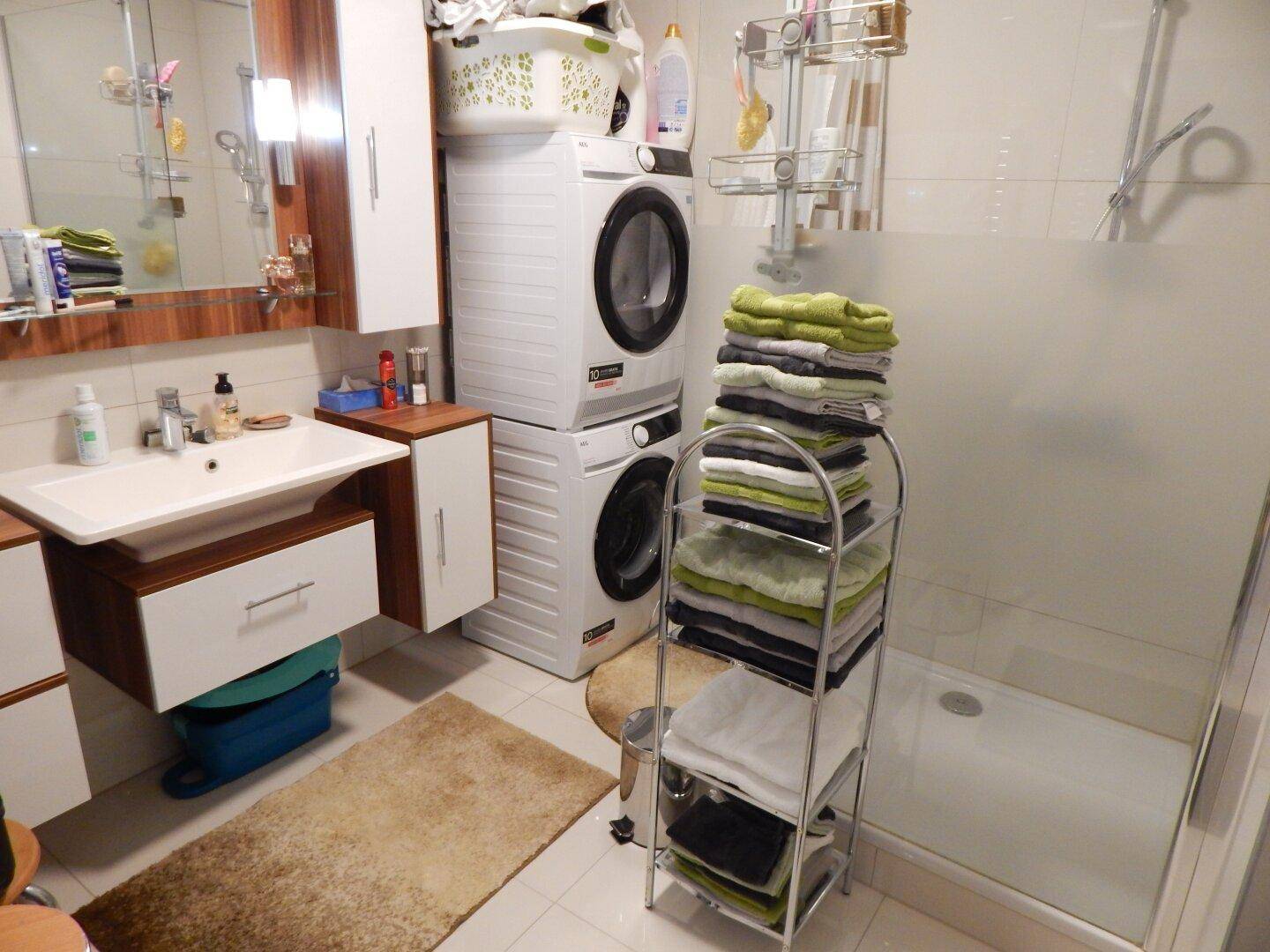 Modernes Badezimmer mit Dusche, Waschbecken und gestapelten Waschmaschinen.