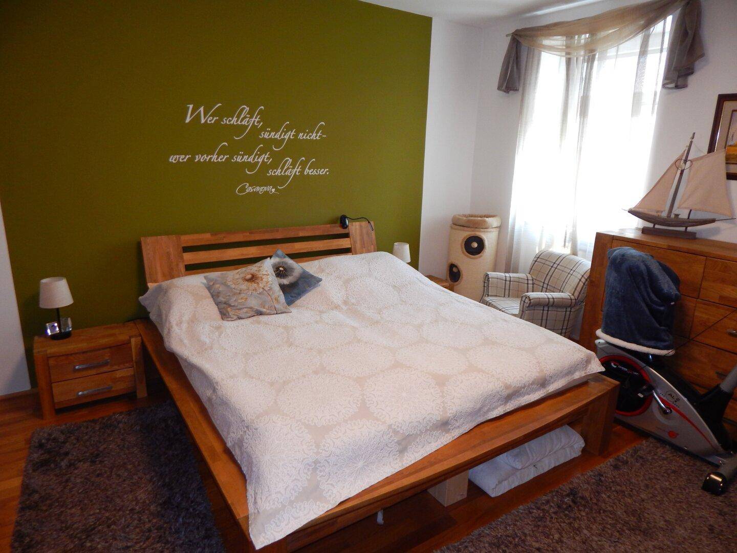 Schlafzimmer mit Holzbett, grüner Akzentwand und Holzboden.