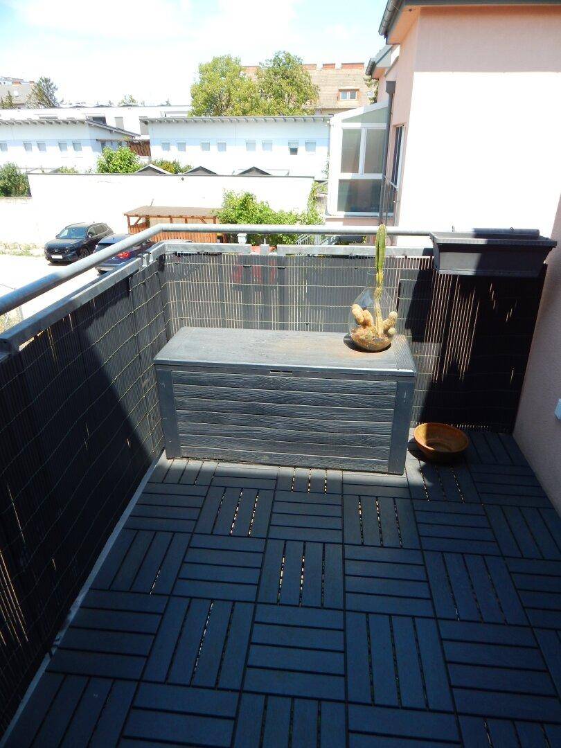 Sonniger Balkon mit dunklen Bodenfliesen und Blick auf die Nachbarschaft.