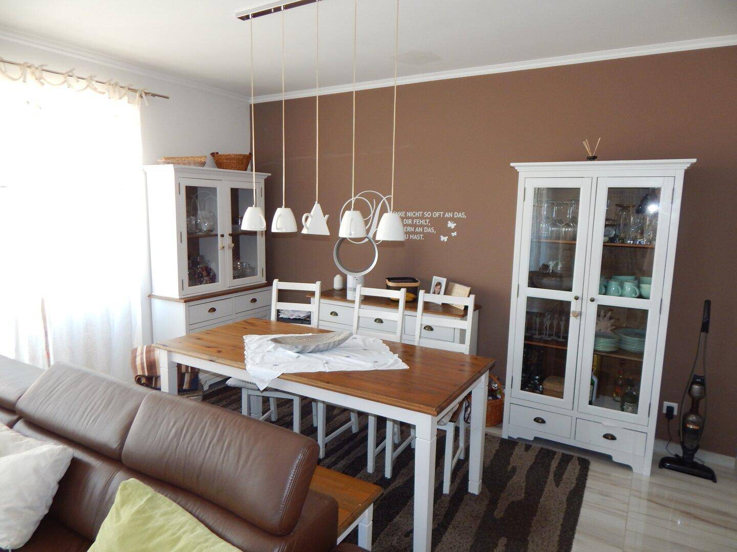 Essbereich mit Holztisch, weißen Vitrinen und brauner Akzentwand.