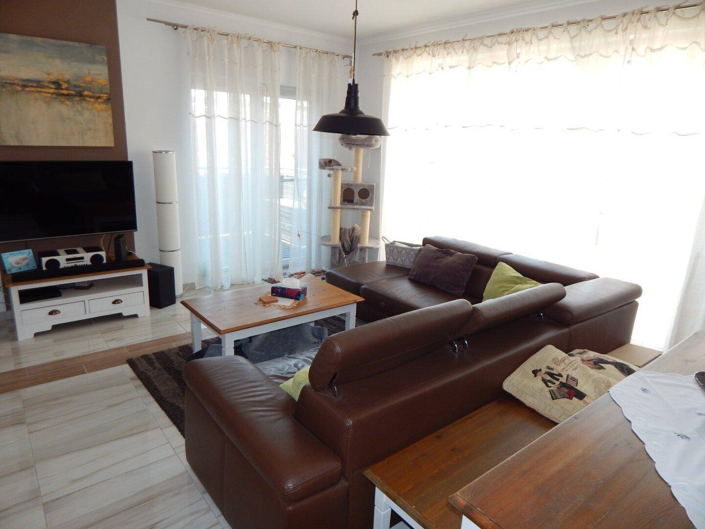 Wohnzimmer mit braunem Ledersofa, Holztisch und Zugang zum Balkon.