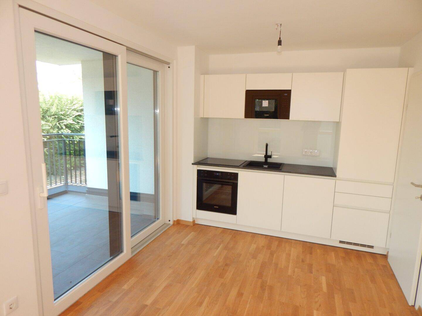 Moderne, helle Küche mit Einbaugeräten, Holzfußboden und direktem Zugang zum Balkon.
