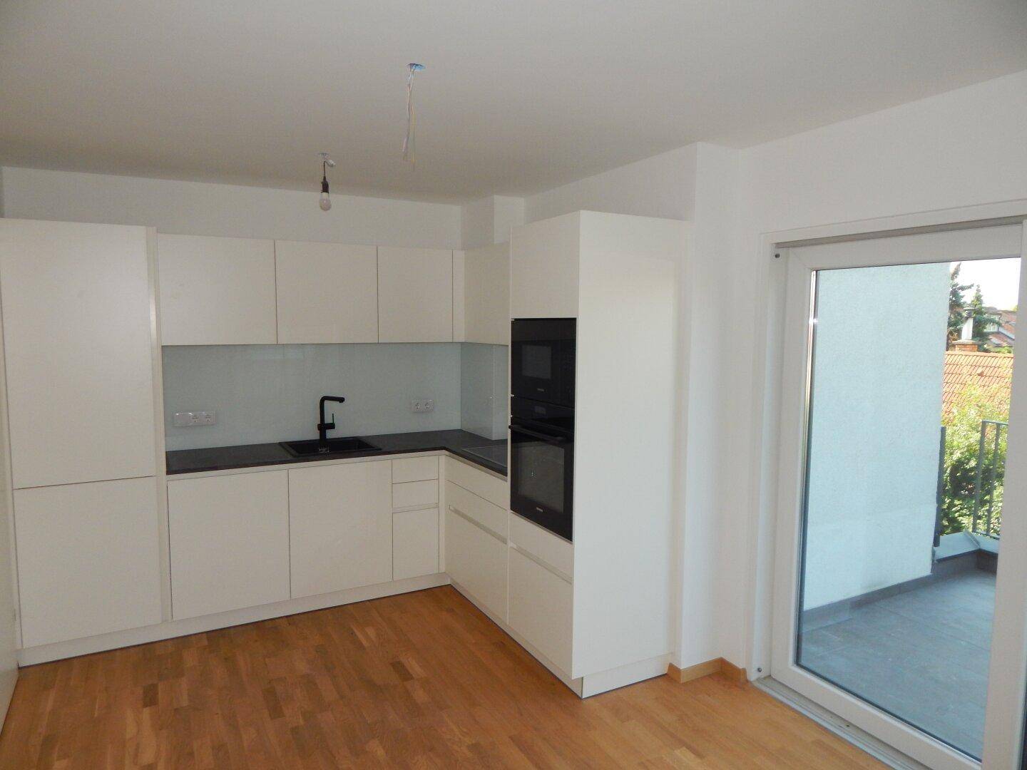 Moderne Einbauküche in Weiß mit dunkler Arbeitsplatte und direktem Zugang zum Balkon.