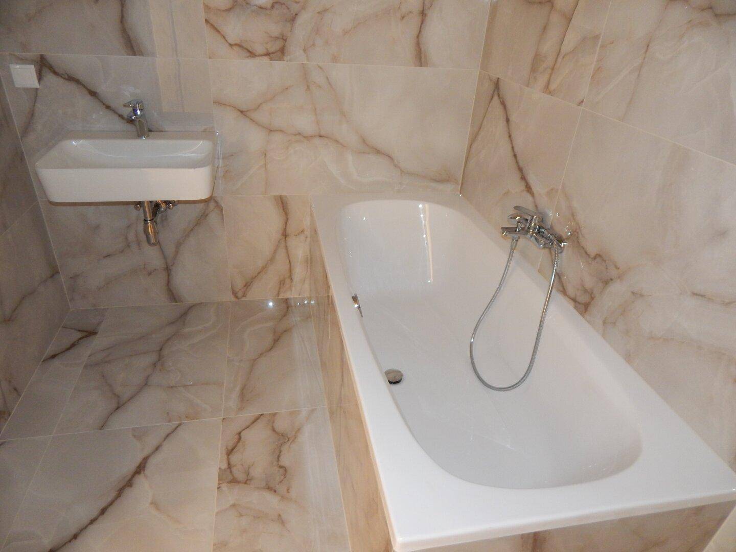 Badezimmer mit beigefarbenen Marmorfliesen, einer Badewanne und einem modernen Waschbecken.