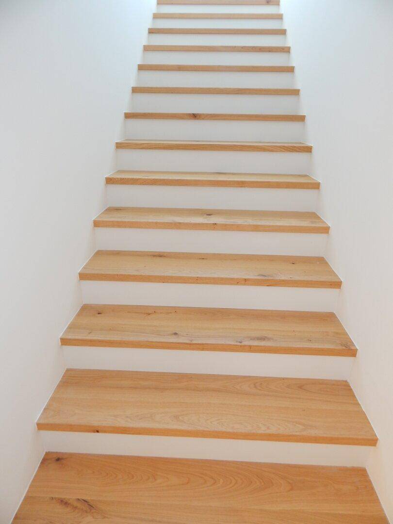 Moderne Holztreppe mit weißen Setzstufen, die in die obere Etage führt.