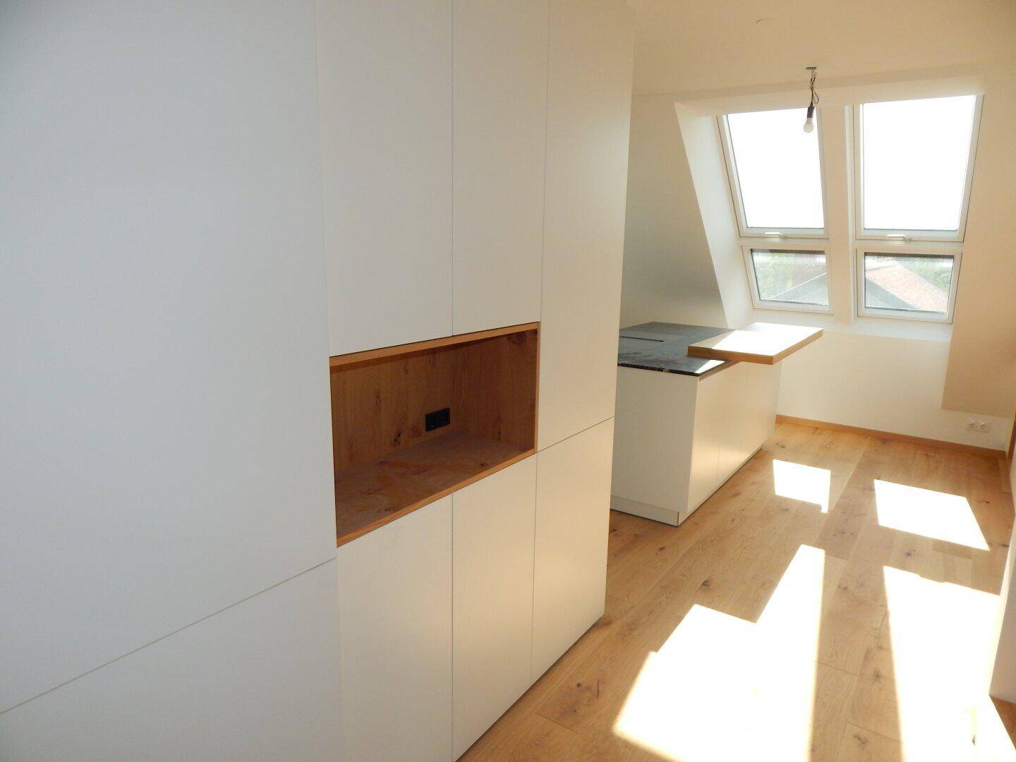Moderner Einbauschrank mit Holzakzenten und Blick auf die Kücheninsel im Dachgeschoss.