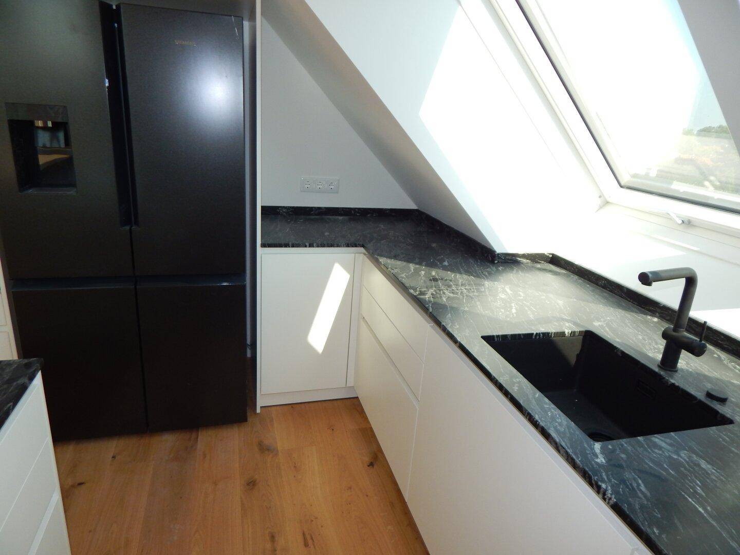Detailansicht der modernen Küche mit schwarzer Spüle, Armatur und großem Kühlschrank.