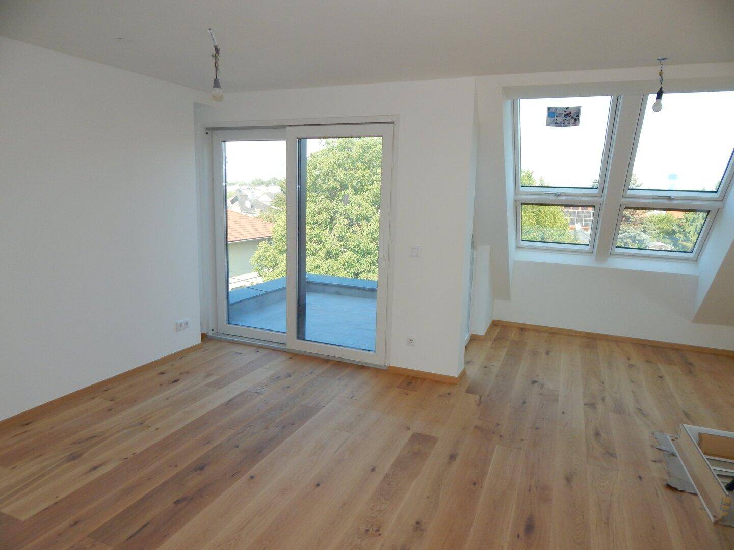 Geräumiger Wohnbereich im Dachgeschoss mit Holzboden, großen Fenstern und Zugang zu einer Terrasse.