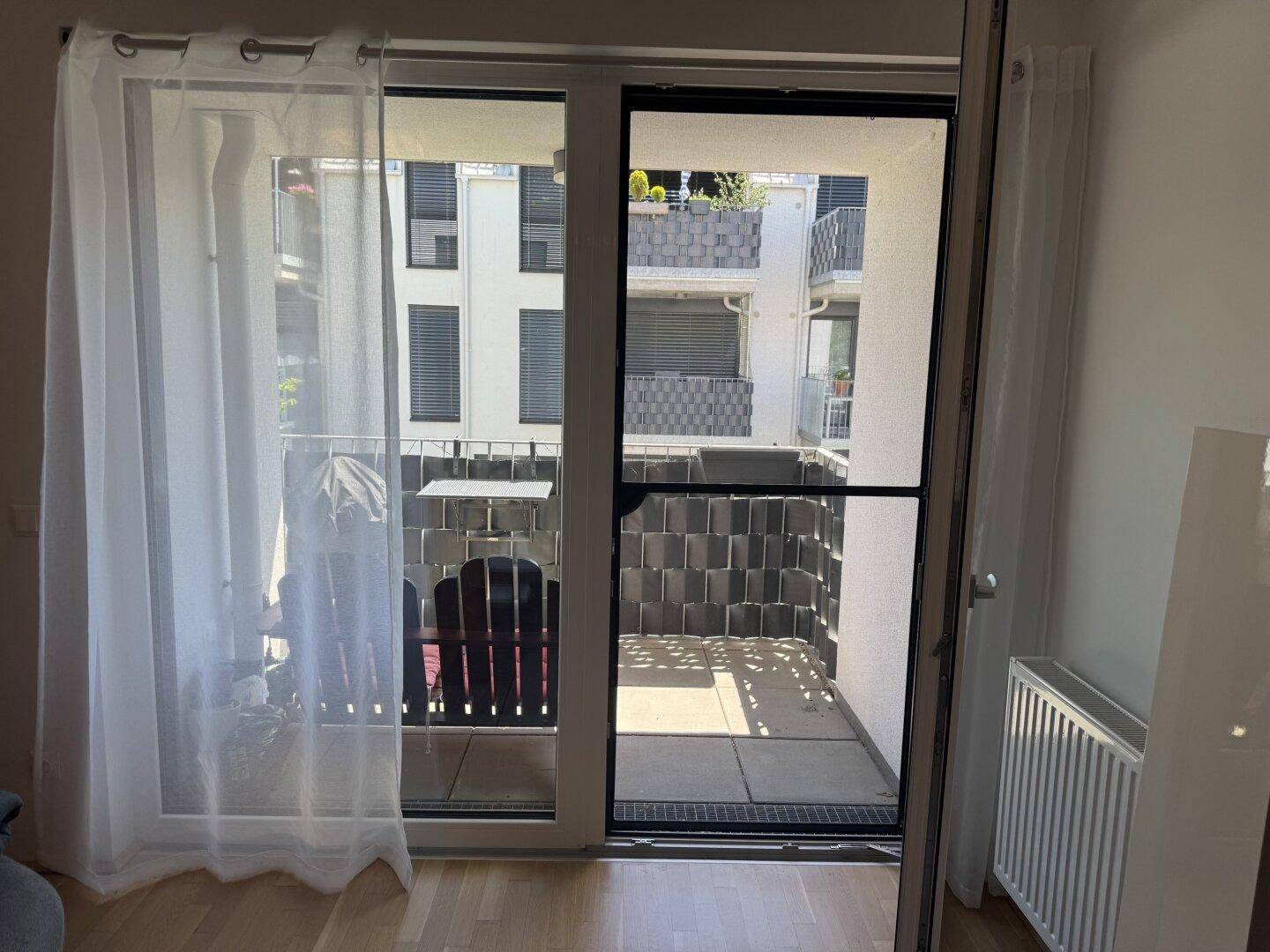 Blick vom Wohnzimmer auf den Balkon mit Sichtschutz und Nachbargebäuden.