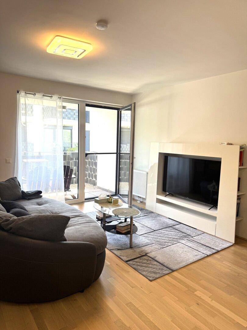 Gemütliches Wohnzimmer mit Sofa, Fernseher und hellem Holzboden.