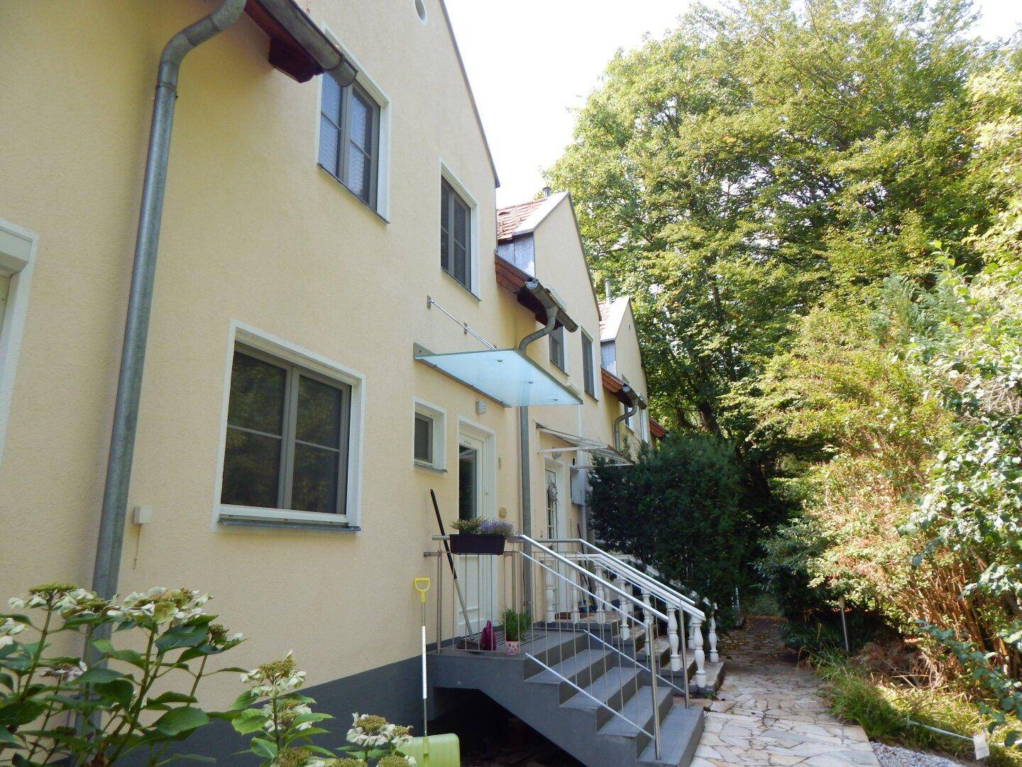 Reihenhausfassade in hellem Gelb mit Fenstern und Treppenzugang zum Eingang.