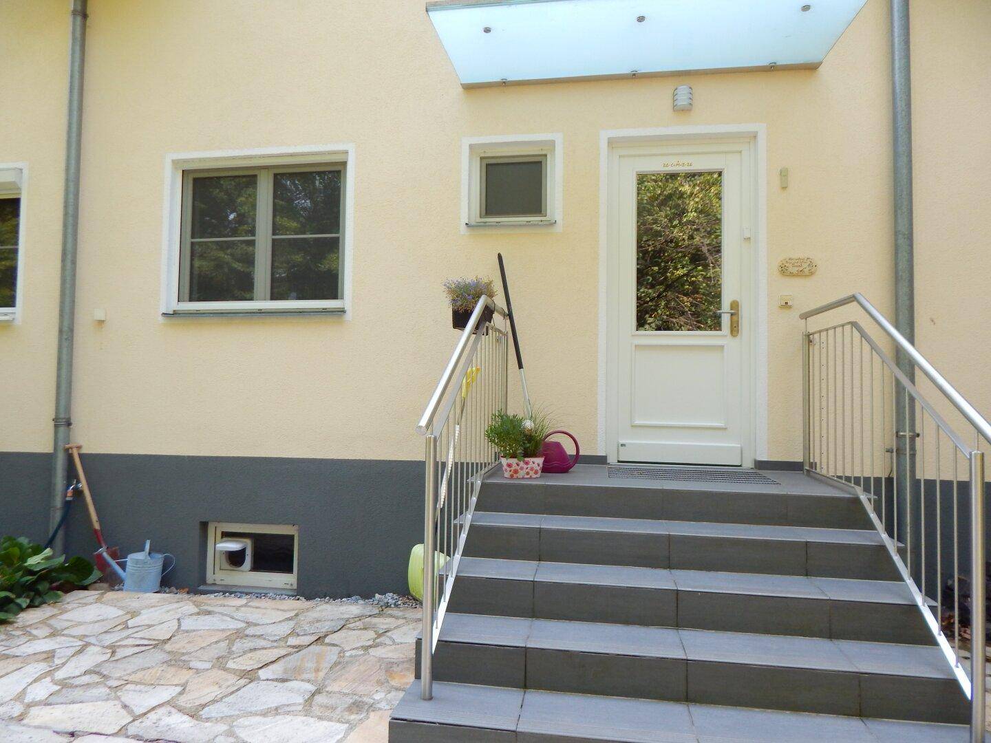 Eingangsbereich eines Hauses mit Treppe, Vordach und heller Fassade.