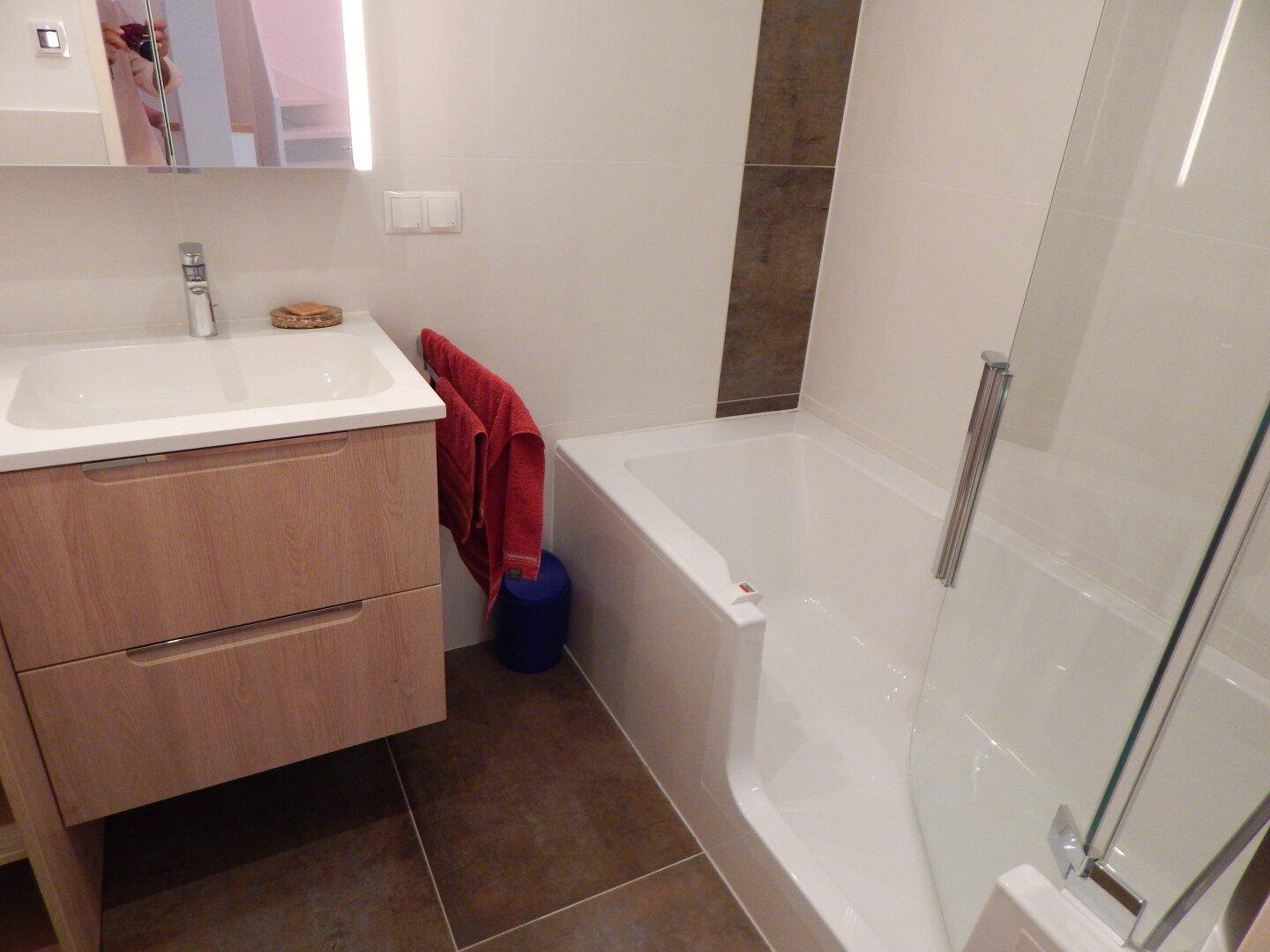 Modernes Badezimmer mit Waschtisch, Badewanne mit Duschwand und Fliesenboden.