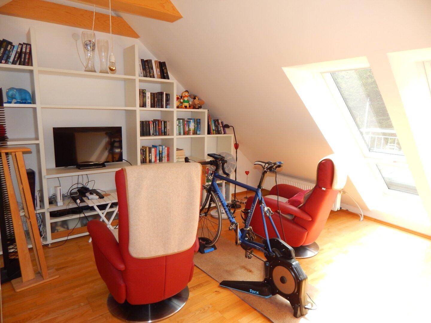 Helles Dachzimmer mit Dachschrägen, Einbauregalen und zwei großen Dachfenstern.