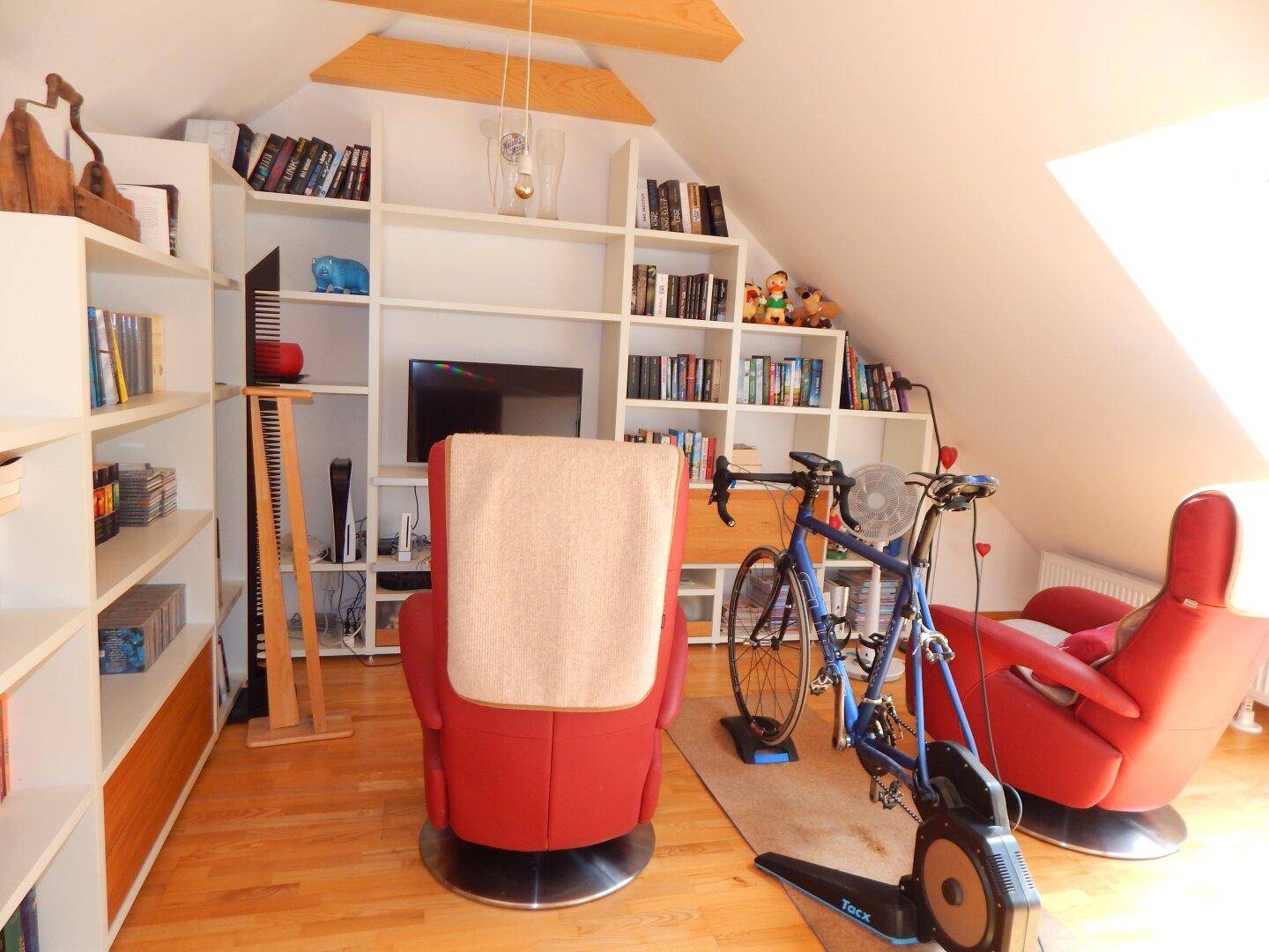 Geräumiges Dachzimmer mit Bücherregalen, Sitzgelegenheiten und viel Tageslicht.