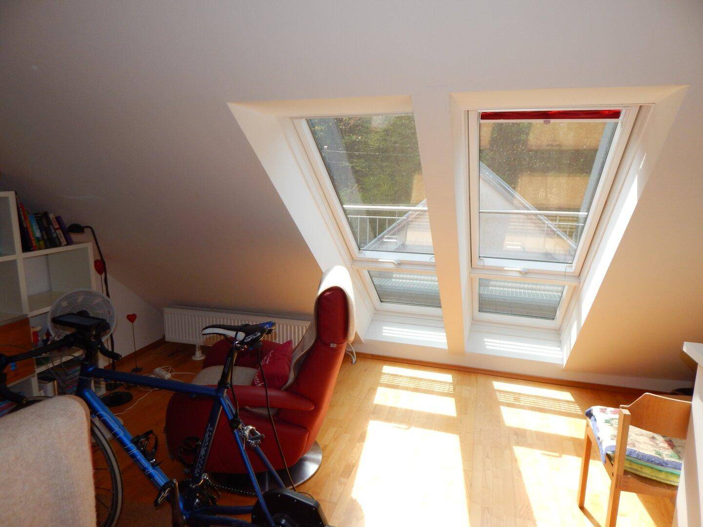 Dachzimmer mit schrägen Wänden und zwei großen Dachfenstern, die viel Licht hereinlassen.