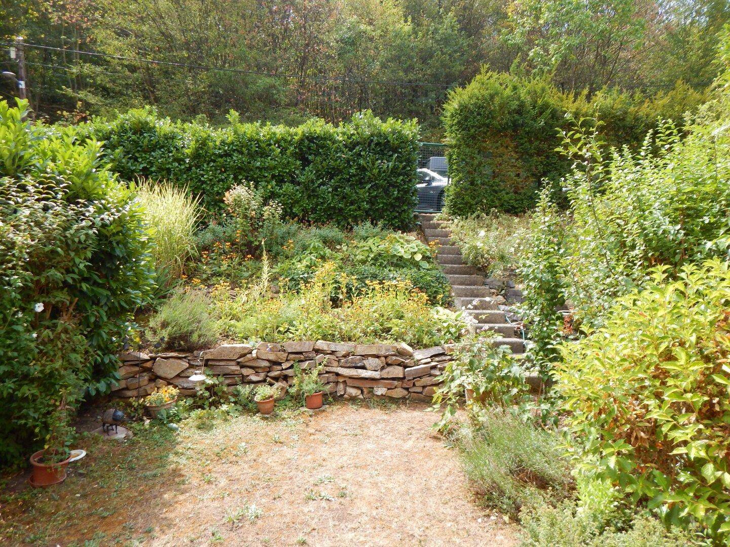 Grüner Garten mit Natursteinmauern und Treppen, umgeben von vielfältiger Bepflanzung.