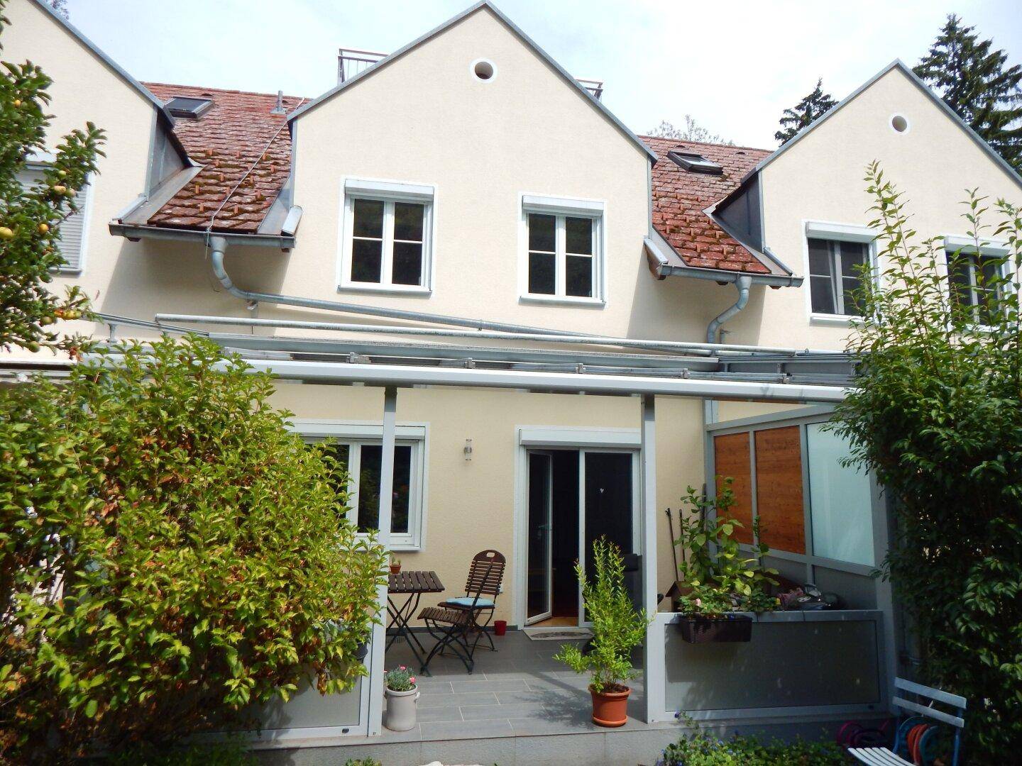Rückseite des Hauses mit einem Wintergarten und einer kleinen Terrasse im Freien.
