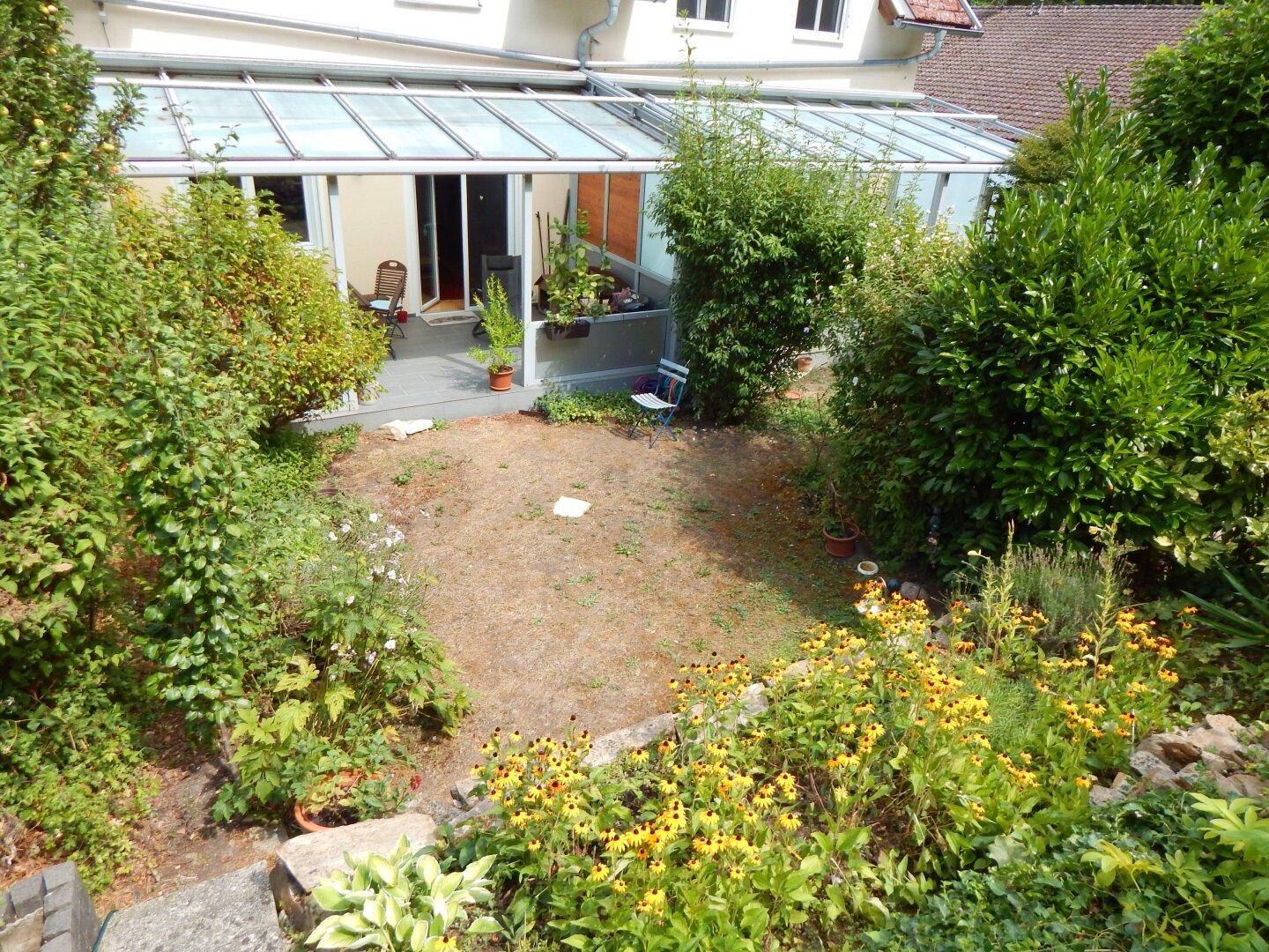 Gartenbereich mit Blumenbeeten und Blick auf das Haus mit dem angrenzenden Wintergarten.