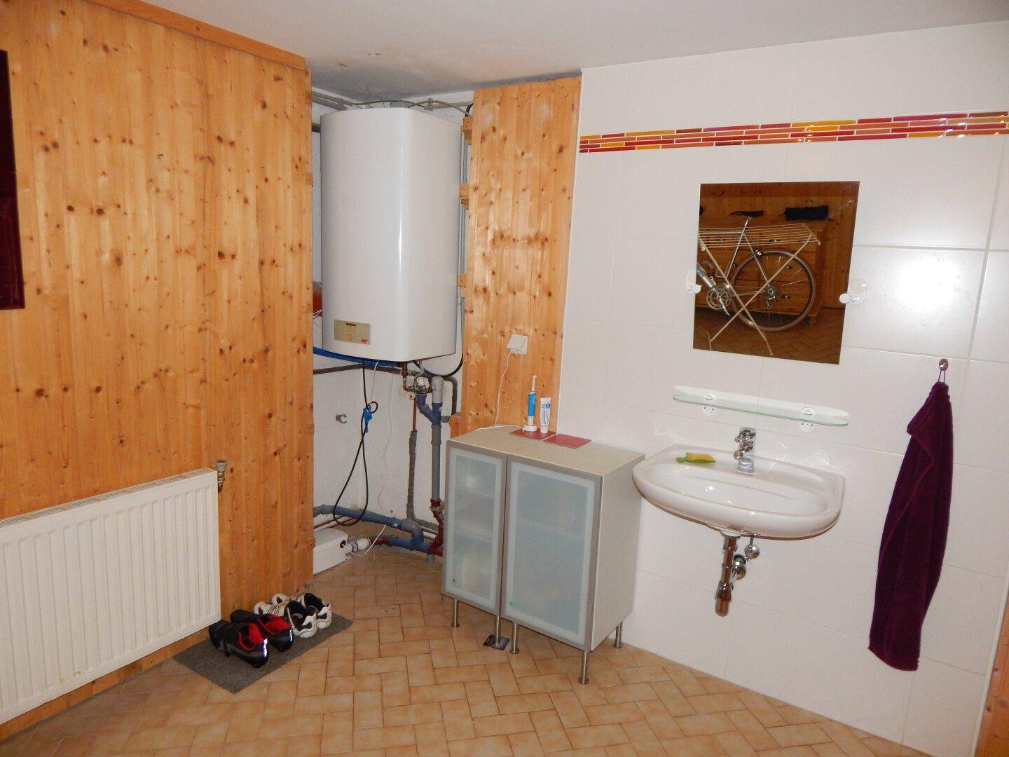 Funktionaler Raum mit Waschbecken, Warmwasserspeicher und Holzverkleidung.