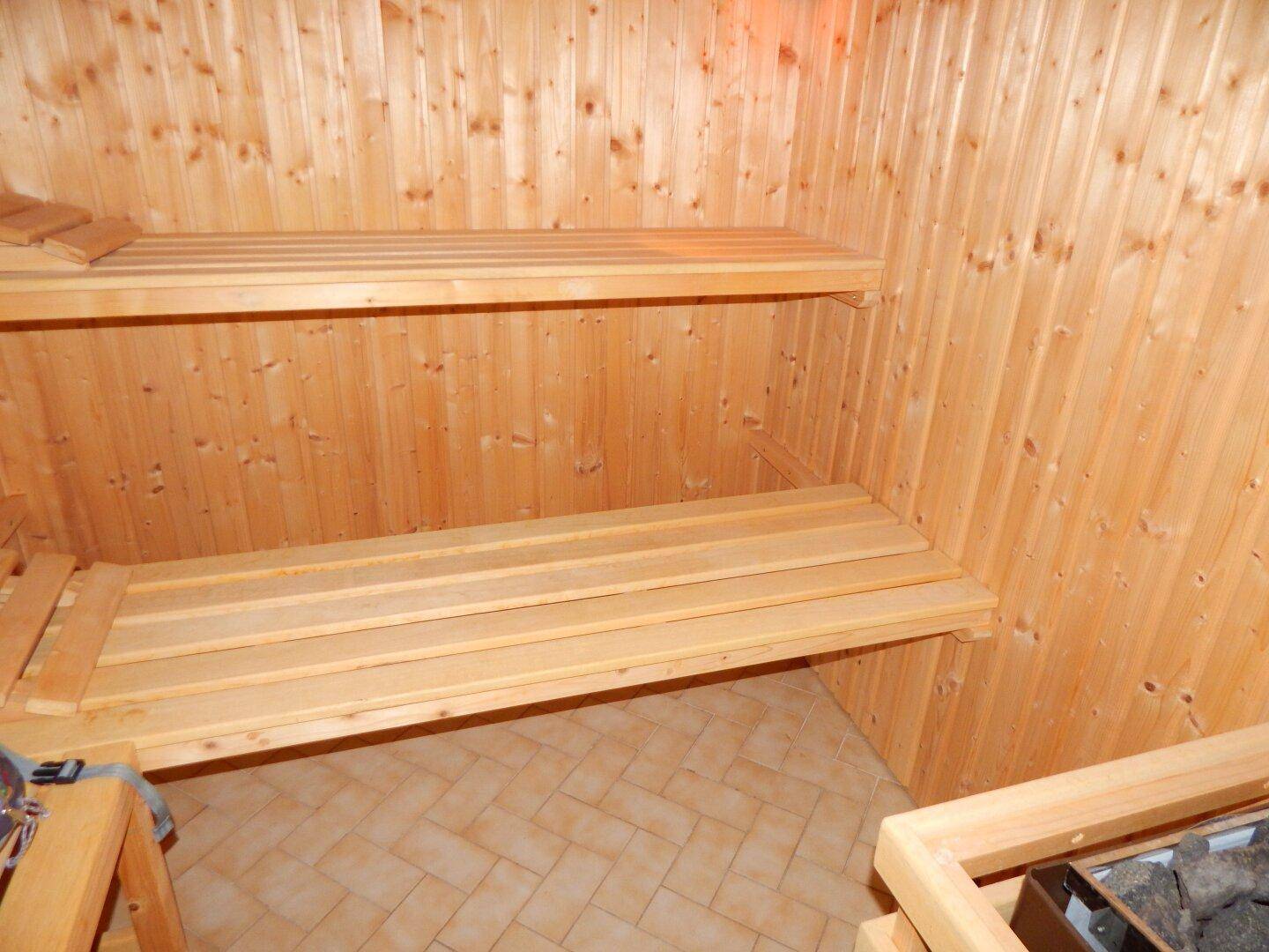 Traditionelle Holzsauna mit zwei Liegeebenen und Fliesenboden für Entspannung.