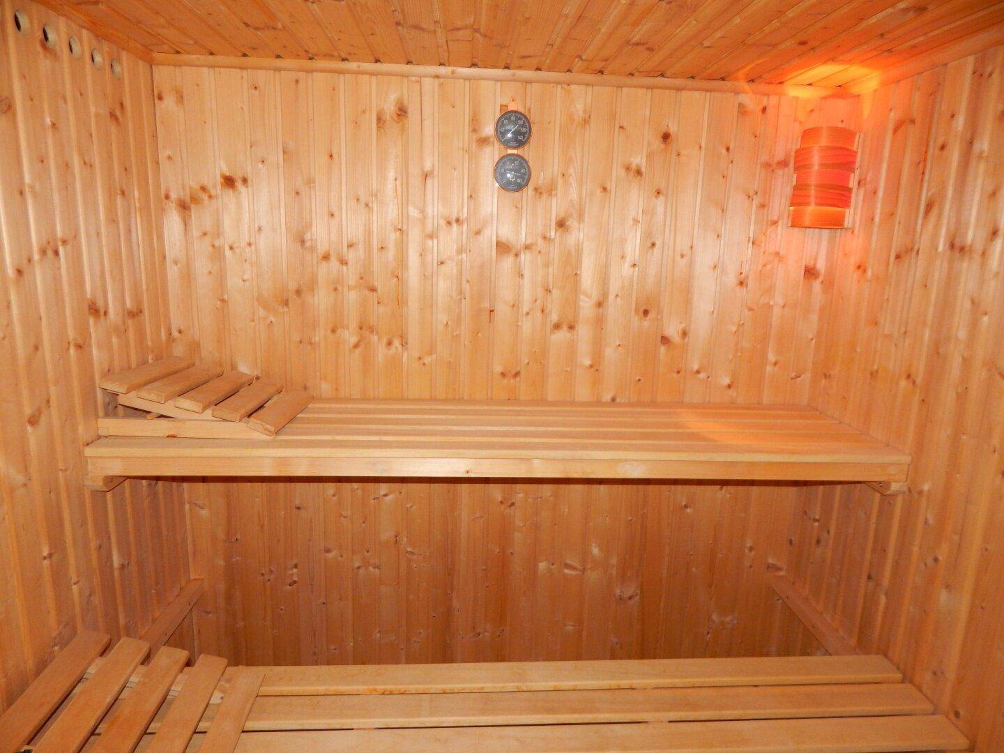 Innenansicht einer Holzsauna mit Bänken und Heizofen für private Wellnessmomente.