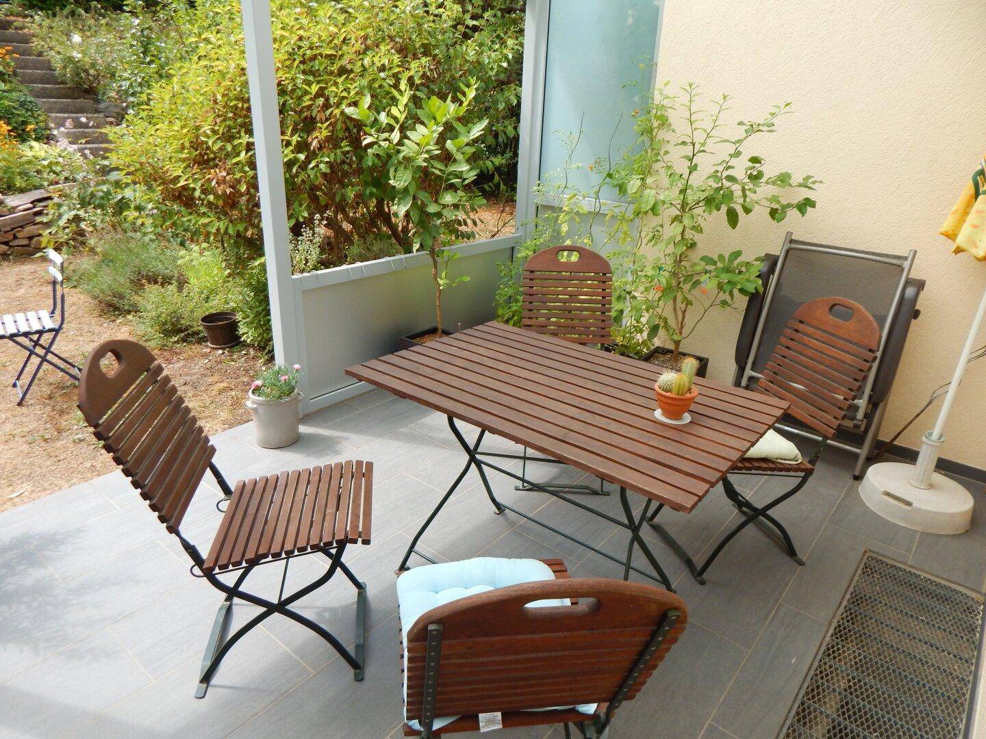 Sonniger Terrassenbereich mit Holztisch und Stühlen, ideal für Mahlzeiten im Freien.