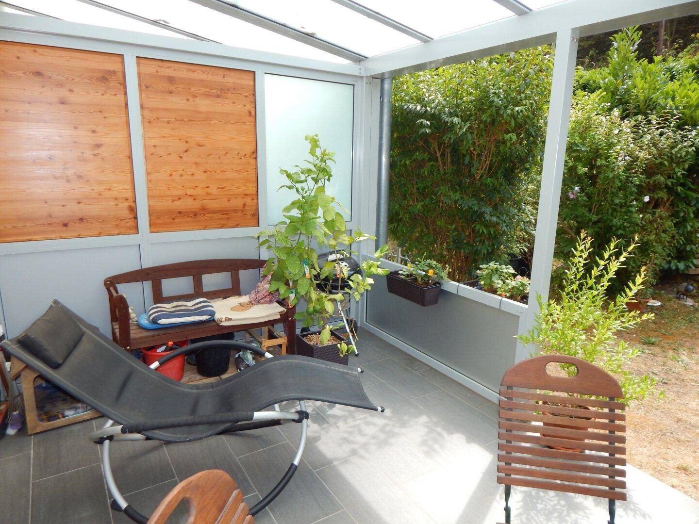 Heller Wintergarten mit Liegestuhl und Bank, bietet einen entspannenden Blick in den Garten.