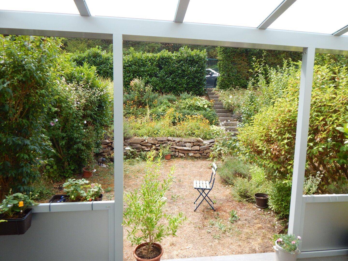 Blick aus dem Wintergarten auf den terrassierten Garten mit üppiger Bepflanzung und Stufen.