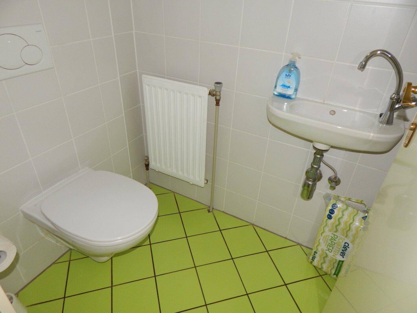Kleines Gäste-WC mit grünen Fliesen, Wand-WC und kompaktem Waschbecken.