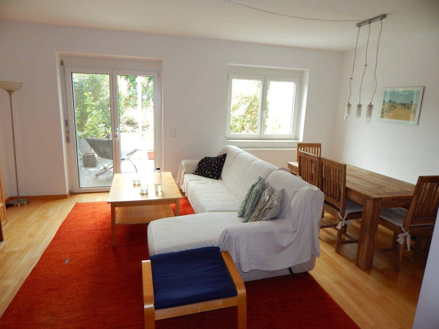 Offener Wohn-Essbereich mit hellem Sofa, Holztisch und direktem Zugang zur Außenterrasse.