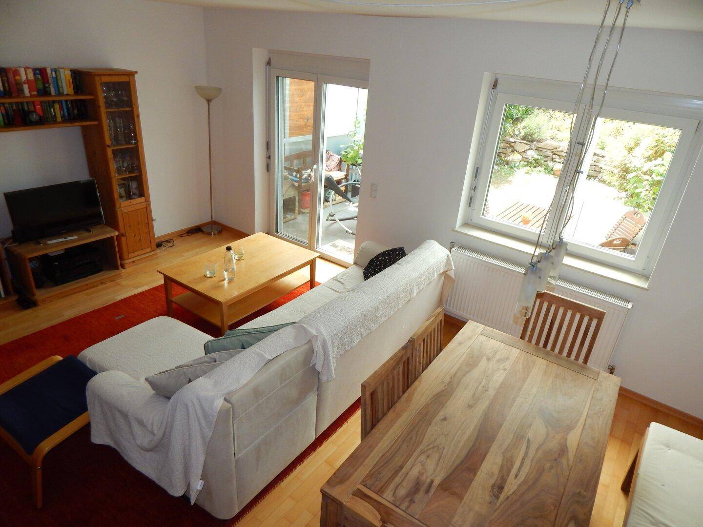 Blick von oben auf den Wohn-Essbereich mit Esstisch und Fenstern zum grünen Garten.