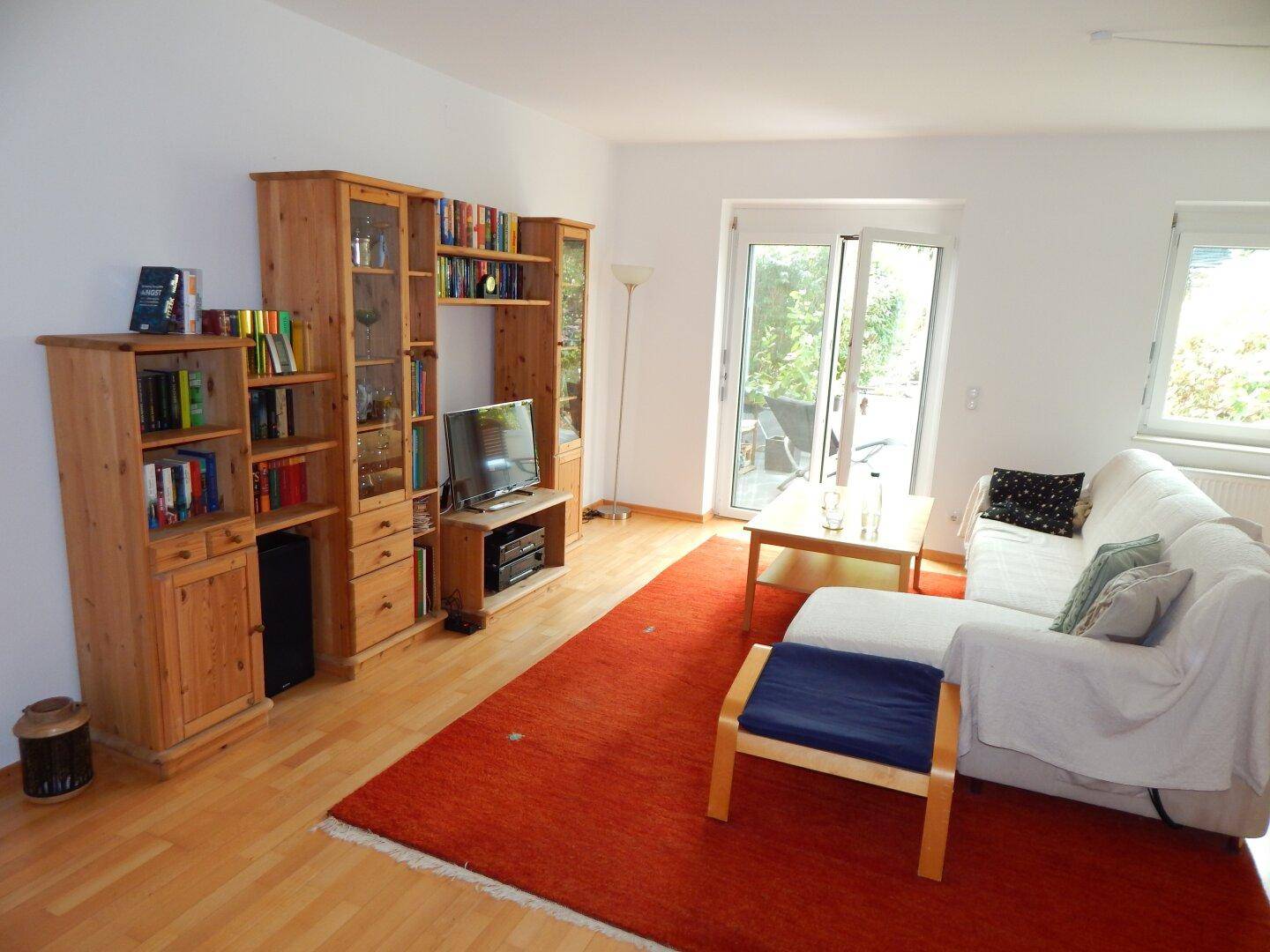 Gemütliches Wohnzimmer mit Holzmöbeln, hellem Sofa und Zugang zu einem Außenbereich.