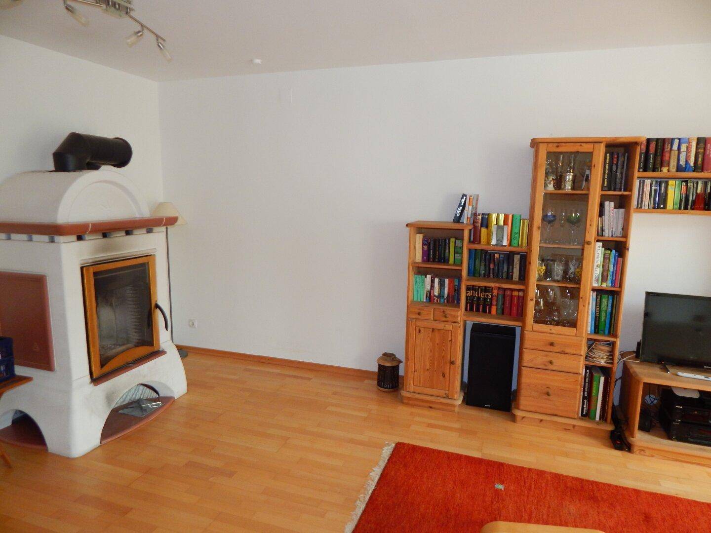 Gemütliches Wohnzimmer mit traditionellem Kachelofen, Holzregalen und Parkettboden.