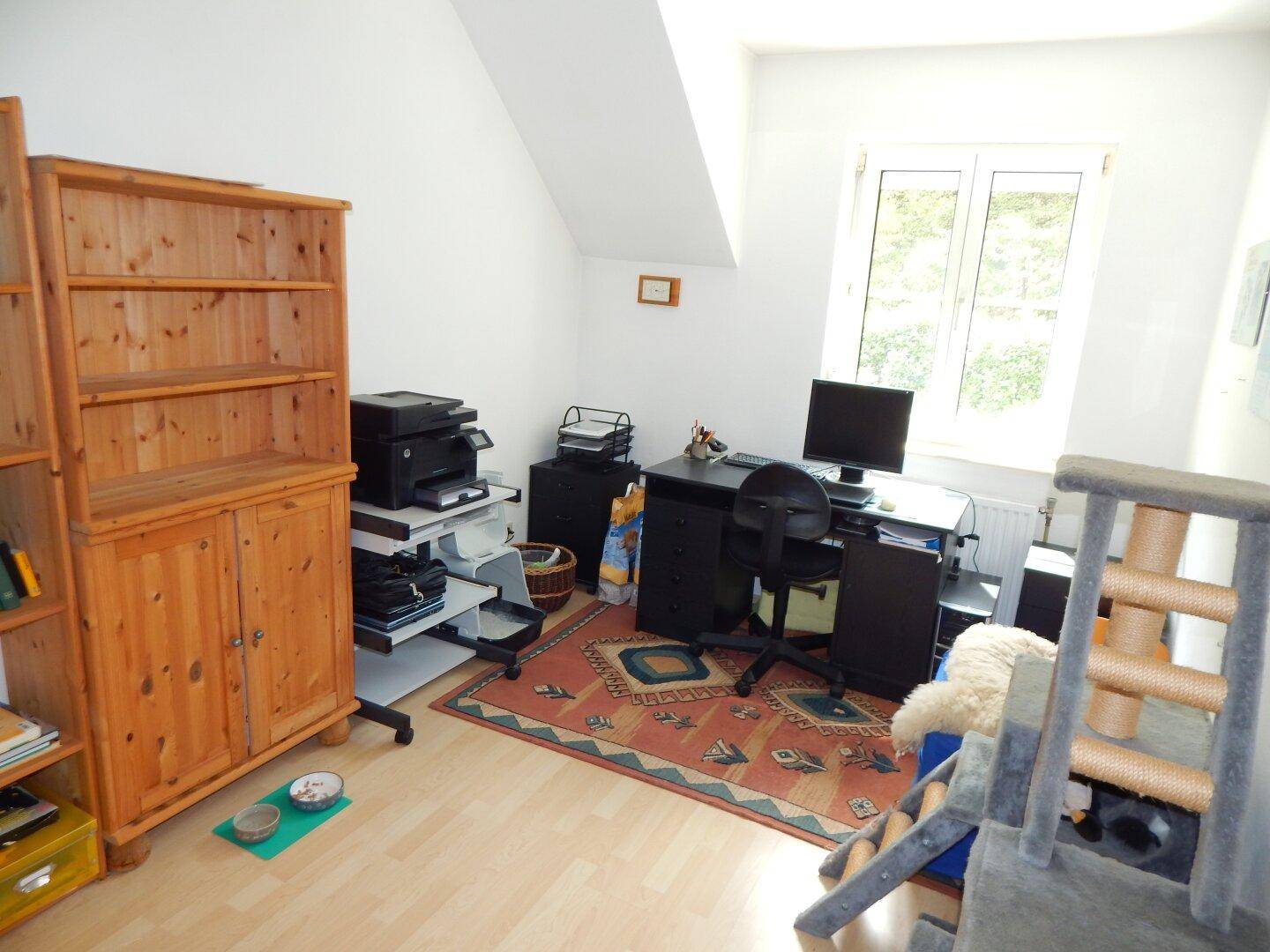 Funktionales Arbeitszimmer mit Holzboden, Schreibtisch und Bücherregal unter der Dachschräge.