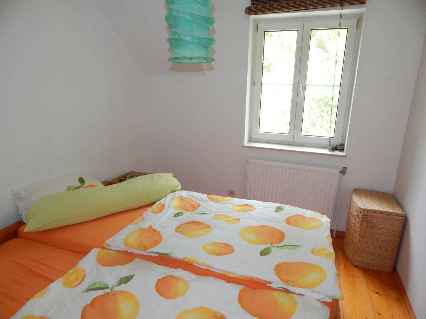 Helles Schlafzimmer mit Holzboden, Fenster und farbenfroher Bettwäsche unter Dachschräge.