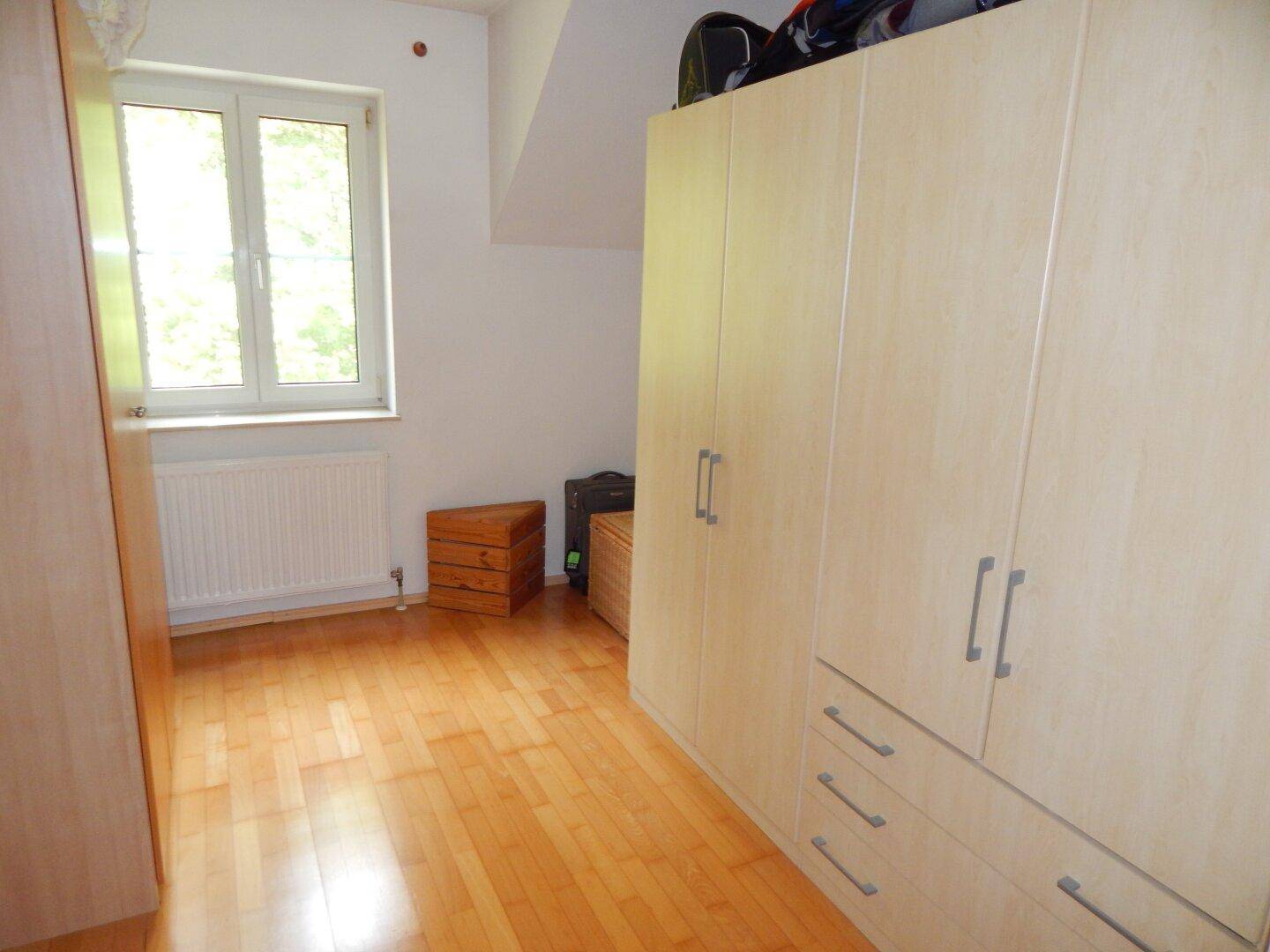 Geräumiges Zimmer mit Holzboden, großem Kleiderschrank und Fenster unter der Dachschräge.