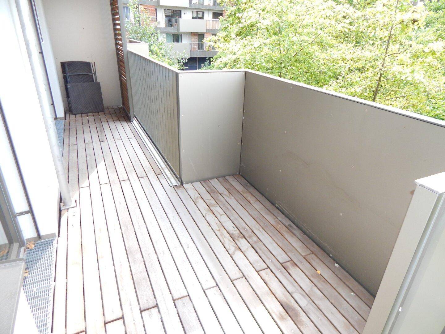 Geräumiger Balkon mit Holzdielenboden und Blick ins Grüne.