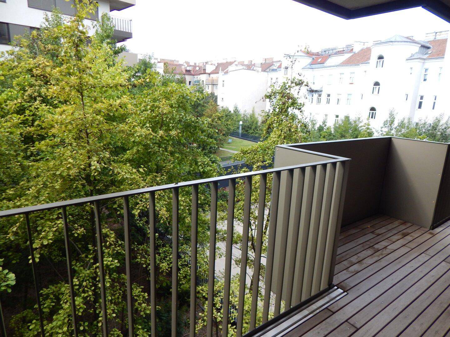Balkon mit Holzboden und weitem Blick auf die umliegende Stadt und Bäume.