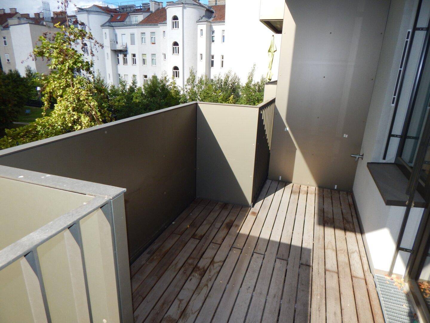 Eckbalkon mit Holzdielen und Blick auf die umliegenden Gebäude und Bäume.