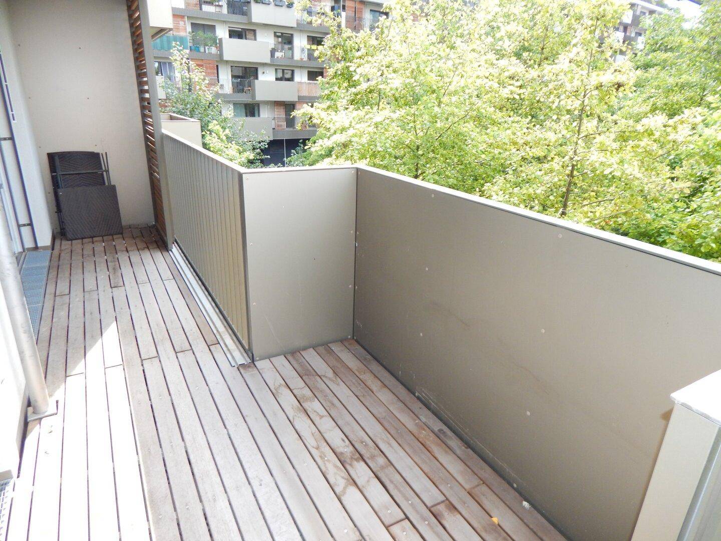 Geräumiger Balkon mit Holzdielenboden und Blick auf den grünen Innenhof.