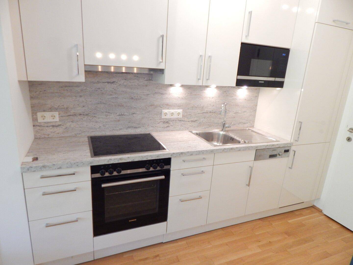 Moderne Einbauküche mit weißen Hochglanzfronten, Induktionskochfeld und Granitarbeitsplatte.