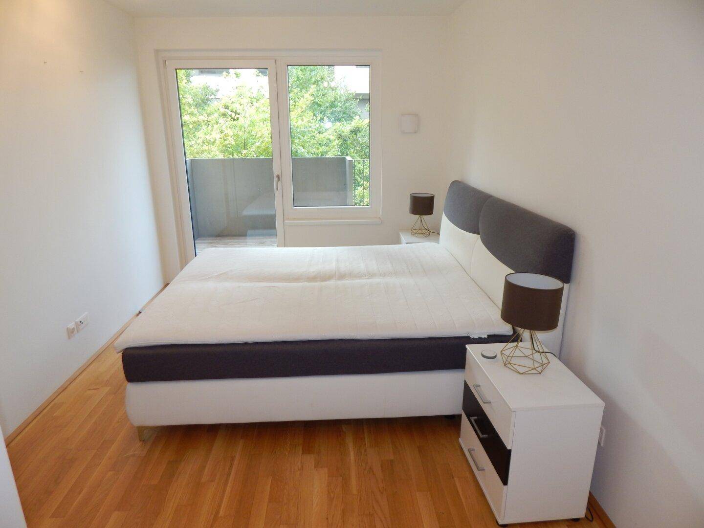 Schlafzimmer mit Doppelbett, Holzboden und Zugang zu einem Balkon mit Grünblick.