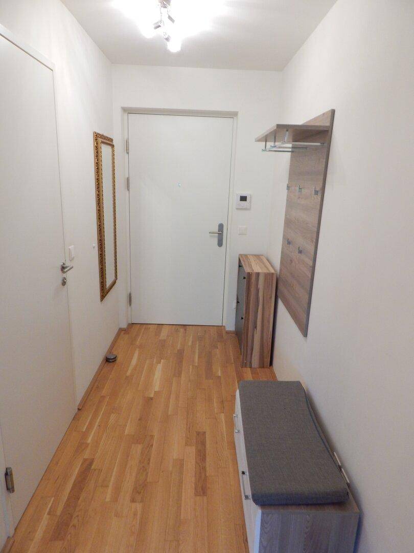 Heller Flur mit Holzboden, Garderobe und Spiegel, führt zum Eingangsbereich.