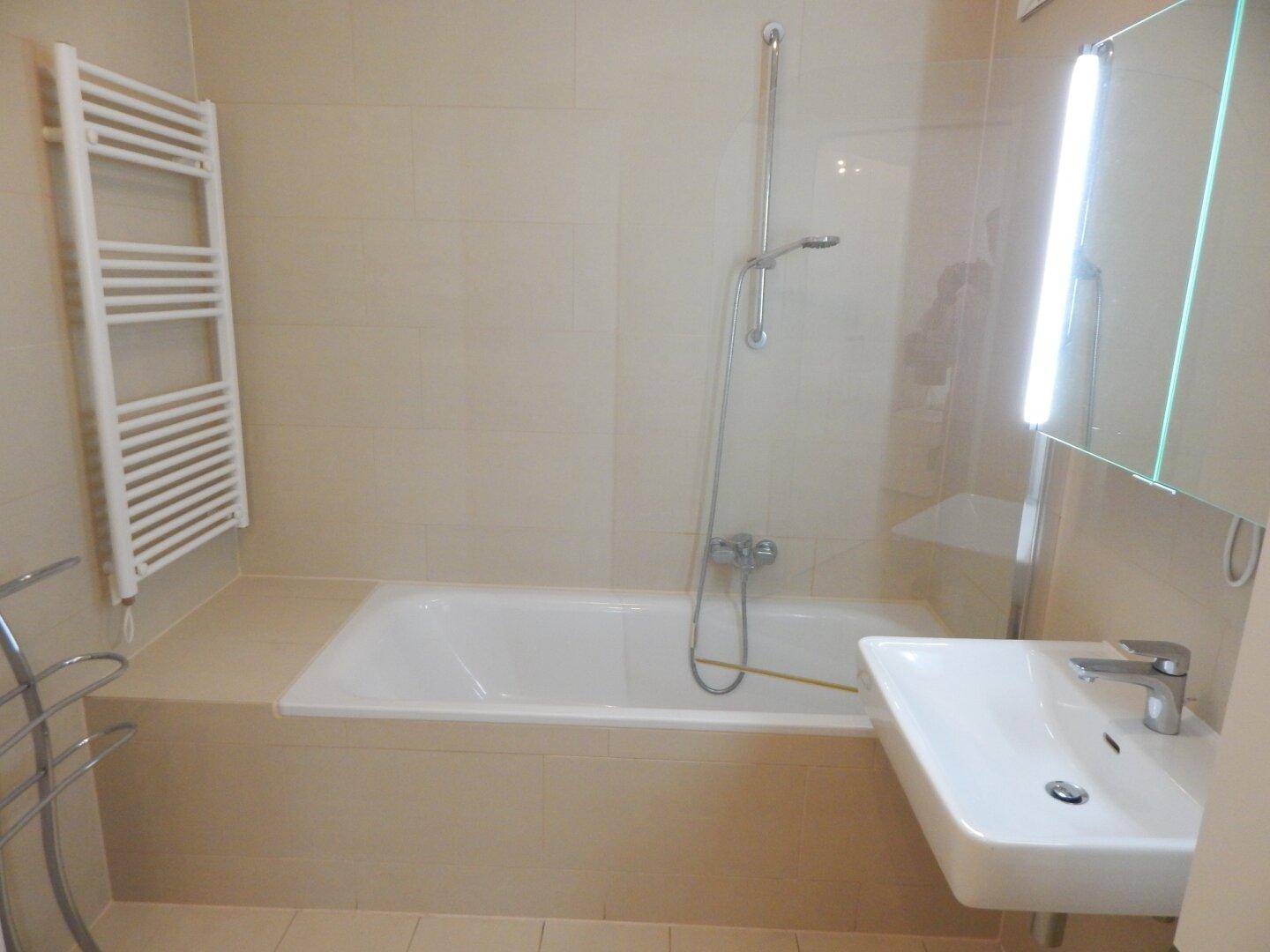 Helles Badezimmer mit Badewanne, Handtuchheizkörper und modernem Waschtisch.